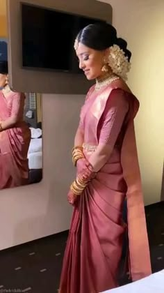 a woman standing in front of a mirror wearing a pink sari and gold jewelry