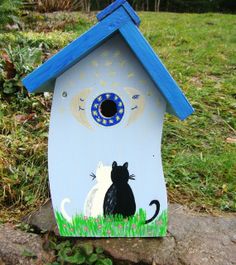 a painted birdhouse with a cat and mouse on the outside, in front of a grassy area