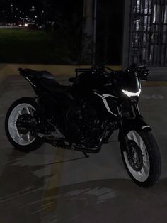 a black motorcycle parked in a parking lot next to a building at night with lights on