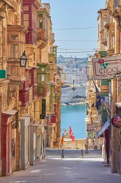 a narrow street with lots of buildings on both sides and a body of water in the distance