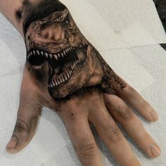 a person's hand with a dinosaur tattoo on it and an evil face painted on the palm