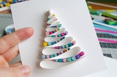 a hand is holding a christmas tree made out of buttons on a piece of paper