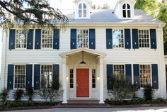 a white house with blue shutters and a red door