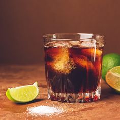 a close up of a drink in a glass on a table with limes and salt