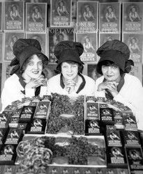 three women in black hats are standing behind a table full of grapes and other items