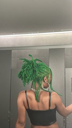 a woman with green dreadlocks is looking at her cell phone in the mirror