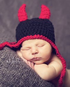 a newborn baby wearing a black and red hat with horns on it's head