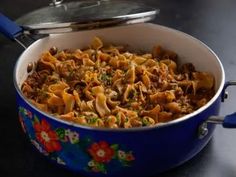 a blue pot filled with pasta and meat on top of a table next to a metal pan