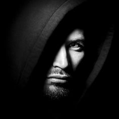 a man with a beard wearing a hoodie looking at the camera in black and white