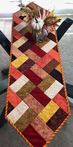 a quilted table runner with flowers in a vase on the top and an ironing board behind it