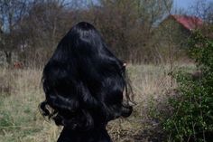 the back of a woman's head with long black hair standing in a field