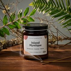 a candle sitting on top of a wooden table next to some plants and leaves in the background