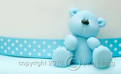 a small blue teddy bear sitting on top of a table next to a polka dot ribbon