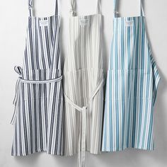 three aprons hanging on a wall with one being tied to the side and another is wearing an apron