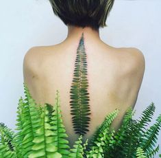 the back of a woman's head with fern leaves on her shoulder and neck