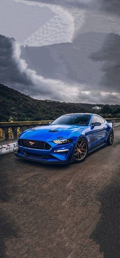 a blue sports car parked on the side of a road with dark clouds in the background