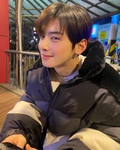 a young man sitting on top of a wooden floor next to a metal railing and wearing a blue jacket