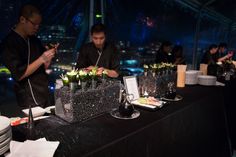 two chefs preparing food on top of a black table in a room filled with people