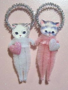 two white cats with blue eyes are standing next to each other holding heart shaped objects