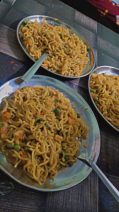 three plates of noodles on a table with silver spoons and two bowls full of them