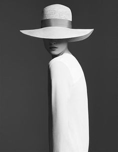 a woman with a hat on her head is standing in front of a black and white background