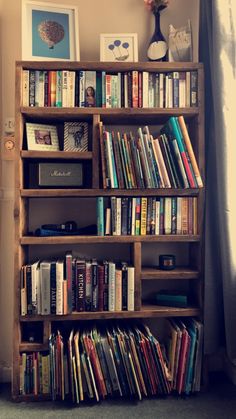 a bookshelf filled with lots of books in front of a window next to a wall