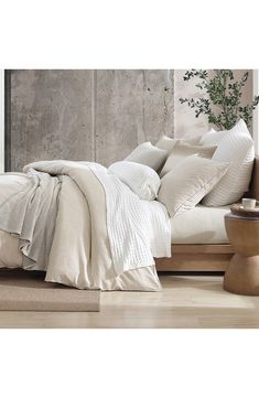 a bed with white sheets and pillows on top of it next to a plant in a vase