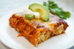 a piece of lasagna on a plate with sour cream and avocado