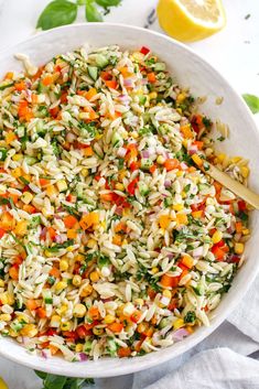 a white bowl filled with pasta salad next to lemon wedges and parsley on the side