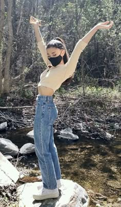 a woman standing on top of a rock next to a river wearing a face mask