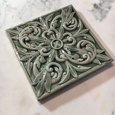 a square tile with an intricate design on it's surface, sitting on a marble countertop