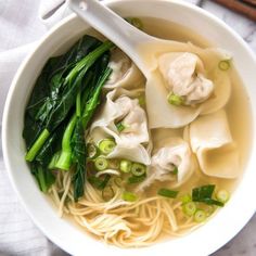 a white bowl filled with noodles, broccoli and dumplings on top of a table