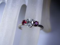 "This is a gorgeous Platinum Diamond and Ruby Ring from Circa 1960s. The center stone is genuine Oval Cut Diamond that is a \"VS\" Quality Diamond. The measurements are 5.5mm by 3.9mm making it just below a half a carat in size and an approximate size of .47 of a Carat. On each side of the center diamond are two lovely round cut genuine ruby gems. Each Ruby measures approximately 3.5mm in size which is approximately .30 in total carat weight (.15 each). This is a very pretty, petite ring with a Oval Three Stone Ruby Ring With Diamonds, Oval Ruby Ring With Three Diamonds, Classic White Oval Ruby Ring, White Oval Ruby Ring, Oval White Ruby Ring, Three Stone Ruby Ring For Anniversary, Oval Sapphire Three-stone Ring For Anniversary, Anniversary Three-stone Oval Sapphire Ring, Anniversary Three Stone Oval Sapphire Ring