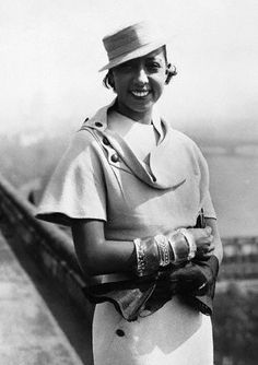 black and white photograph of a woman wearing a hat with gloves on her hands, smiling at the camera