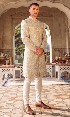 a man standing in front of an archway wearing a beige sherve and white pants