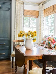 sunflowers are in a white vase on a table next to a window with drapes