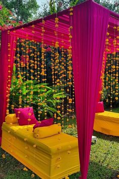 a yellow and pink bed sitting under a canopy in the grass next to trees with flowers hanging from it