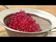 a strainer filled with red beads on top of a wooden table