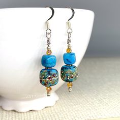 These turquoise blue glass dangle earrings feature handmade lampwork beads with stone, crystal, and silver bead accents. The main glass beads have subtle golds, purples, and dots of silver on a turquoise blue background. The main glass beads have a matte finish and have a feel similar to ceramic. The turquoise blue bead is semi-precious crazy lace agate.  I only made one pair of these earrings - they are truly one of a kind! They are roughly 2 inches long and the widest bead is roughly 1/2 inch Artisan Blue Beaded Earrings As Gift, Blue Earrings With Spacer Beads For Gift, Handmade Turquoise Beaded Earrings With Czech Glass, Adjustable Turquoise Earrings With Spacer Beads, Artisan Blue Beaded Earrings, Turquoise Czech Glass Earrings As Gift, Turquoise Round Beaded Earrings, Turquoise Beaded Earrings With Colorful Czech Glass, Artisan Blue Jewelry With Dangling Beads