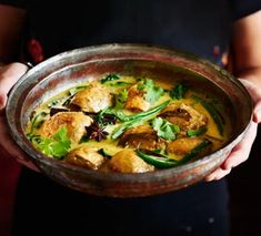 a person holding a metal bowl filled with food and garnished with green leaves