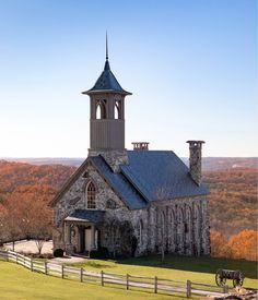 an old stone church with a steeple surrounded by autumn trees and rolling hills in the background