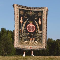 a person holding up a large tapestry with skulls and pomegranates on it