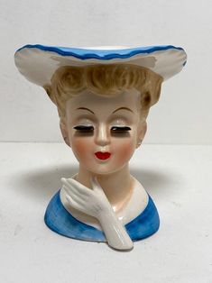 a ceramic figurine wearing a blue and white hat with her hand under her chin