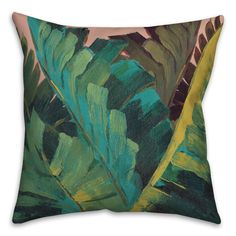 a green and yellow pillow with large leaves on the front, sitting on a white surface