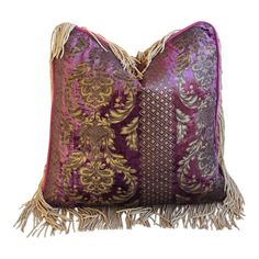 a purple and gold pillow with tassels on the bottom, sitting against a white background