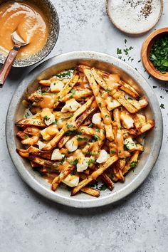 a bowl filled with french fries next to bowls of sauce and seasoning on the side