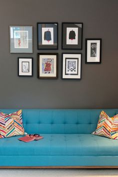 a blue couch sitting in front of a wall with framed pictures on it's sides