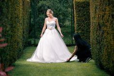 a woman in a white wedding dress standing next to a person kneeling on the ground