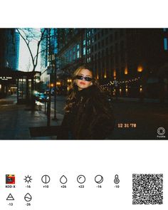 a woman wearing sunglasses standing in front of a tall building at night with buildings and street lights behind her