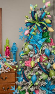 a christmas tree decorated with blue, green and pink ornaments is in the corner of a room